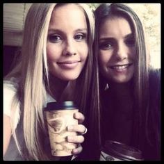 two beautiful young women sitting next to each other holding coffee cups in front of them