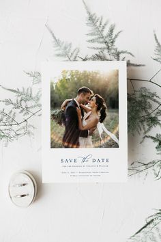 save the date card with an image of a bride and groom kissing in front of greenery