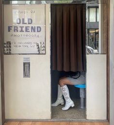 a woman is sitting in the doorway of an old friend photo booth with her boots on