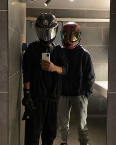 two people wearing helmets are taking a selfie in a bathroom mirror with their cell phones