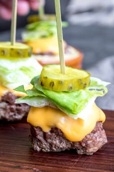 two hamburgers with pickles and cheese on them are sitting on a wooden table