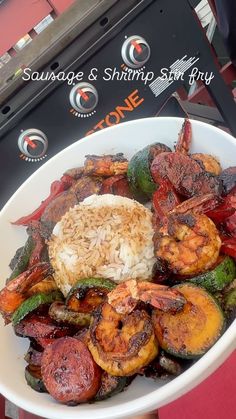 a white bowl filled with shrimp, rice and veggies on top of a red table