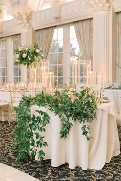 the table is set up with white linens and greenery for an elegant wedding reception