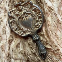 an antique looking mirror is laying on a lace covered table cloth with the image of a heart in it