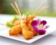 some food on a white plate with purple flowers and chopsticks in the foreground