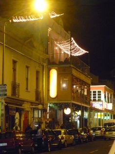 a city street at night with cars parked on both sides and lights strung over the buildings