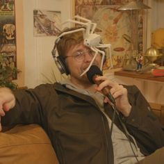 a man sitting on a couch wearing headphones and holding a microphone to his ear