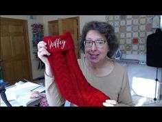 a woman holding up a red knitted stocking with the word dolly written on it