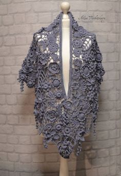 a white mannequin wearing a gray crocheted shawl on top of a brick wall