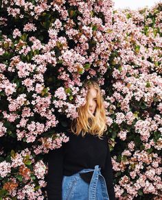 a woman standing in front of a bush with lots of pink flowers on it's side