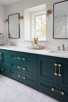 a bathroom with green cabinets and gold handles on the sinks, along with two mirrors