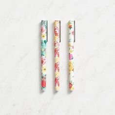 three pens sitting next to each other on a white surface with floral designs in them