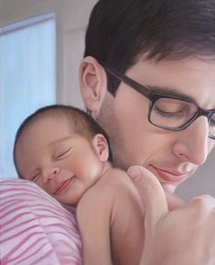 a man holding a baby in his arms and smiling at the camera while wearing glasses