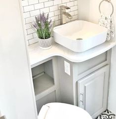 a white bathroom sink sitting under a mirror next to a toilet and counter top with a potted plant on it