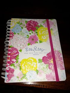 a notebook with flowers on it sitting on top of a wooden table next to a pen