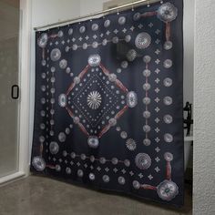 a black shower curtain with silver and red designs on it in a bathroom next to a glass door