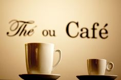 two coffee cups sitting on top of saucers in front of the sign for the ou cafe