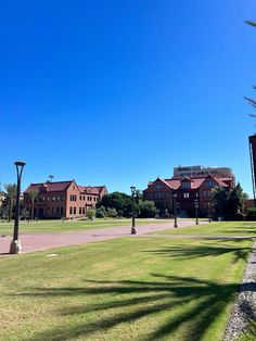 an empty park with lots of grass and street lights in the foreground, on a sunny day