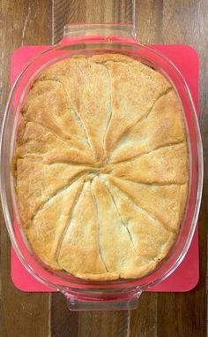 a pie sitting in a glass dish on top of a wooden table next to a red napkin