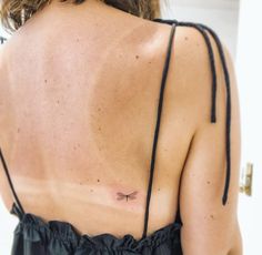 the back of a woman's dress with a dragonfly tattoo on her left shoulder