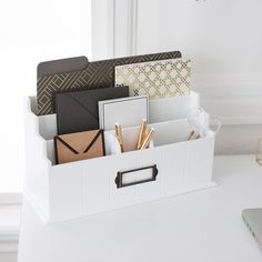 a white desk with an open file box and various office supplies in it, along with a laptop on the table