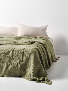 an unmade bed with two pillows on top of it and a green blanket over the headboard