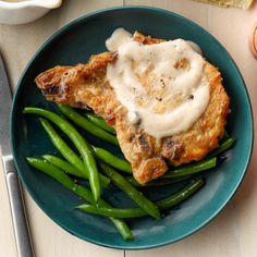 a blue plate topped with green beans and chicken covered in gravy on top of it