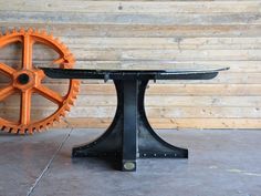 an orange and black table sitting next to a large gear wheel on top of a wooden wall