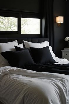 a bed with black and white pillows in a bedroom next to a window, near a night stand