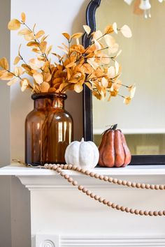 a fireplace mantel with pumpkins and flowers in vases next to a mirror