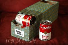 two cans of soup are sitting in a box on a red couch with the lid open