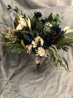 a bridal bouquet with blue flowers and greenery on a gray sheeted bed