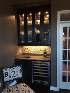 a small kitchen with black cabinets and wine glasses on the cabinet door, next to a chair