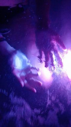 two hands touching each other in front of purple and blue lights on a dark background