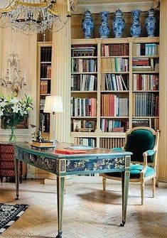 the room has many bookshelves and chandeliers, including an antique desk