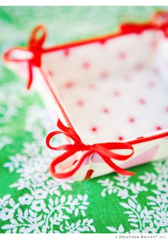 a small white box with a red bow on it sitting on a green and white tablecloth