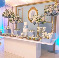 a table topped with lots of white and blue cakes next to tall vases filled with flowers