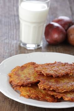 some food on a white plate next to a glass of milk and plums in the background