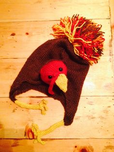 a knitted hat with a red and yellow bird on it's head sitting on top of a wooden floor