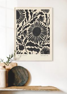 a black and white floral print on a wall above a wooden shelf next to a potted plant