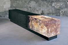 a marble bench sitting in front of a stone wall and cement floored room with concrete walls