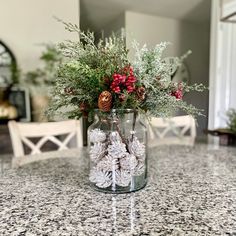 a glass vase filled with flowers and pine cones on top of a marble countertop