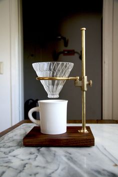 a coffee cup sitting on top of a wooden stand next to a glass pouro