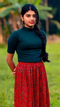 a woman in a green shirt and red skirt posing for the camera with her hands on her hips