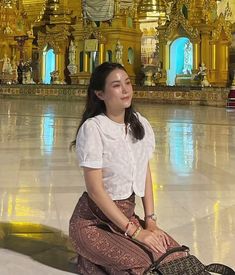 a woman sitting on the floor in front of a building with gold pillars and arches