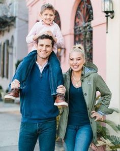 a man, woman and child posing for a photo in front of a pink building