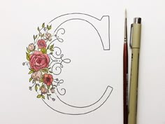 the letter c is decorated with flowers and leaves on white paper next to a pen