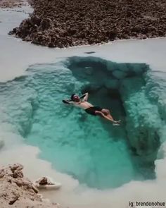 a man is swimming in the water near some rocks and ice formations that look like they are melting