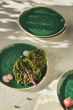 two green plates with radishes on them sitting on a white cloth covered table