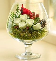 a glass vase filled with white flowers and a red bird sitting on top of it